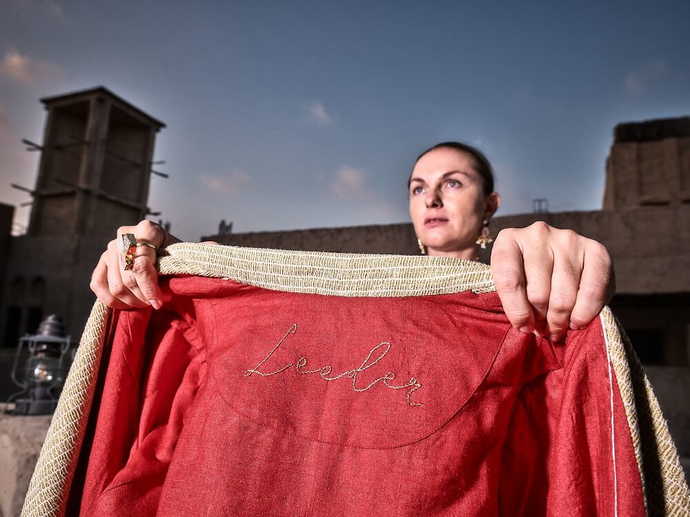 Woman holding a coat from the signature collection of Kashesh Global with 'Leader' embroidery against a rustic background