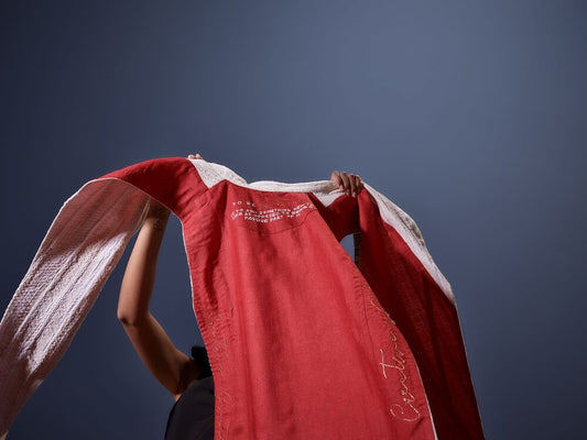 Red Kashesh Global cape with white embroidery held by a person against a dark background | Luxury Dubai Women's Fashion